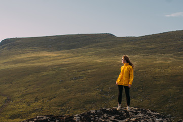 Fototapeta premium Girl in yellow jacket staying in mountains and looking to fjord