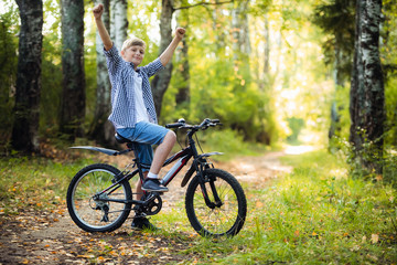 Fototapeta na wymiar Boy riding a bike outdoors in the grass on a sunny day with hands raised