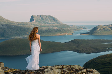 Back of girl in wedding dress staying in mountains and looking to fjord - 299201895