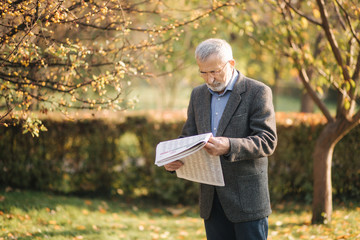 Senior man read a newspaper in the park. Background of yellow tree in autumn