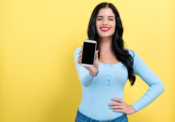 Young woman holding out a cellphone in her hand on a yellow background