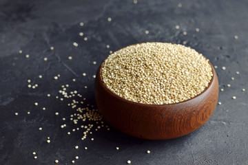 Quinoa grains in wooden bowl on black concrete background