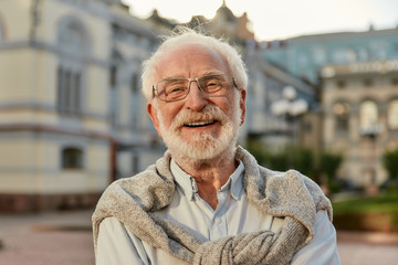 Forever young. Portrait of handsome bearded senior man in glasses looking at camera and smiling while standing outdoors