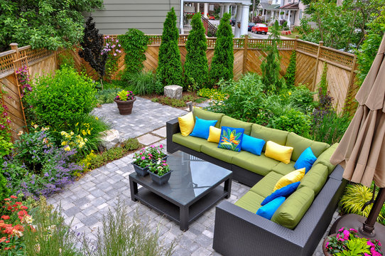 A beautiful small, urban backyard garden featuring a tumbled paver patio, flagstone stepping stones, and a variety of trees, shrubs and perennials add colour and year round interest. 
