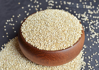 Organic quinoa grains in wooden bowl on black concrete background
