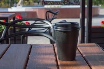 Hot coffee in a paper Cup on a table in a street cafe