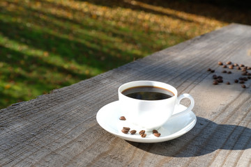 Close up top view high key a white cup of black coffee with coffee beans on the wooden table. Colourful bokeh from natural morning sunlight and bright autumn background.