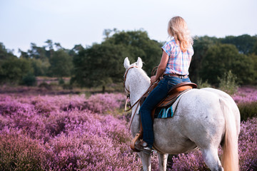 Frau sitzt auf ihrem weißen Pony während eines Ausrittes im Westernsattel in der Heide und schaut...
