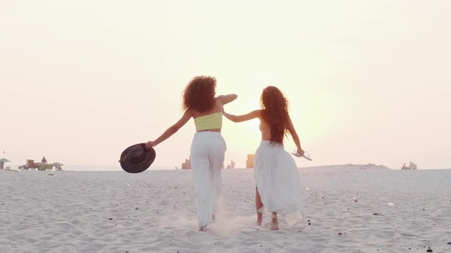 Two beautiful curly-haired girls together on the beach. Concept of homosexual couple or friends traveling together. Cinematic 4K.