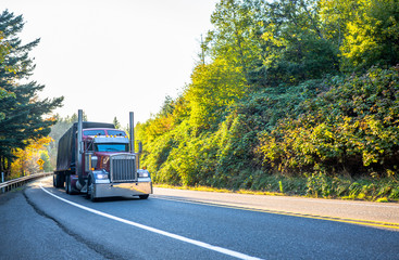 Big rig powerful classic semi truck transporting covered cargo on flat bed semi trailer  moving on...