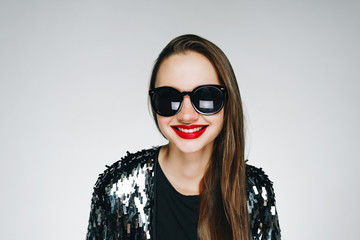 fashionable brunette with bright lipstick in sunglasses on a gray background smiles wide