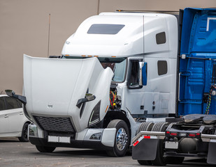 Big rig semi truck tractor standing on the parking lot with open hood for engine inspection and maintenance