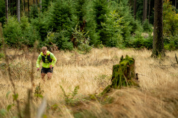 Young athlete runs uphill with a drinking backpack. Trail run in a beautiful autumn forest