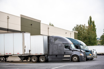 Big rig semi trucks with semi trailers standing in the warehouse dock loading cargo for next delivery