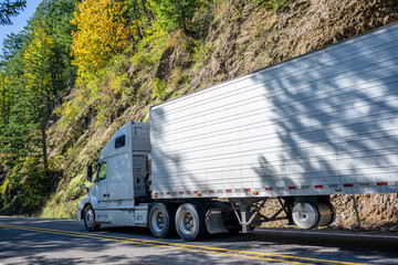 Big rig white semi truck transporting cargo in refrigerator semi trailer running on the mountain...