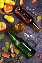 Bottles and glass of apple and pear cider with fruits and leaves on black background. Overhead vertical image