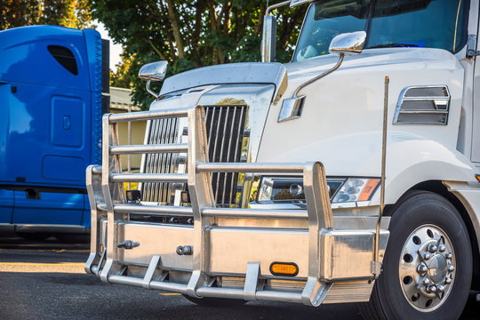 Bright white big rig semi truck tractor with aluminum grille guard bumper standing in row on truck stop