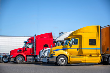 Different big rigs semi trucks with semi trailers standing in row on truck stop parking lot for truck drivers rest and adherence to the transportation schedule © vit