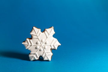 gingerbread cookie of snowflake on blue background. Traditional Christmas food. Christmas and New Year holiday concept. Copyspace
