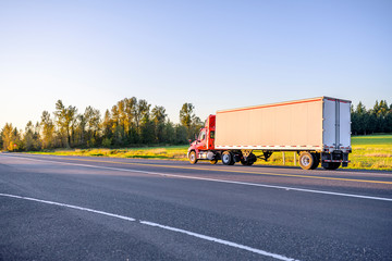 Red big rig day cab semi truck transporting cargo in dry van semi trailer running on the sunny local road © vit