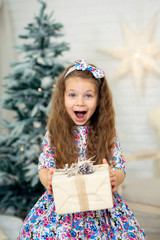 portrait of a cute little girl in a beautiful dress surprised holding a box with a Christmas present in her hands