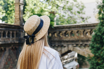 A thin blonde girl with long hair in a white dress stands with her back to the camera and looks...