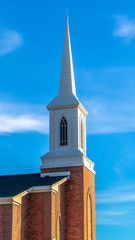 Vertical frame Close up of church exterior with steeple and red brick wall against blue sky