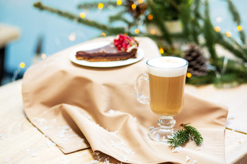 Delicious fresh festive morning cappuccino coffee in a glass cup and cupcake dessert on the wooden table, fireflies and spruce branches