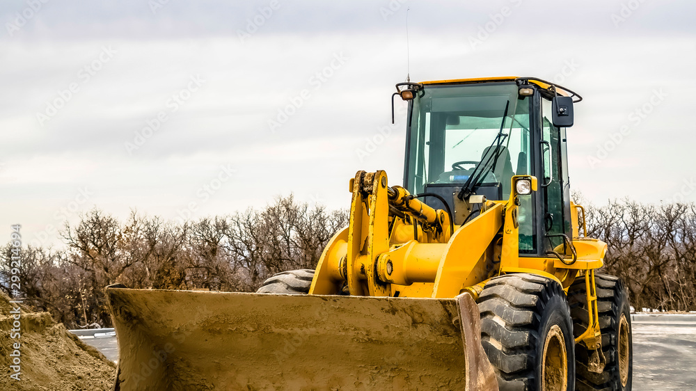 Wall mural Panorama Focus on a yellow bulldozer with dirty bucket and wheels at a construction site