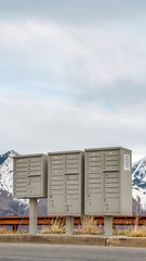 Obraz premium Vertical frame Selective focus mailboxes beside a road against snowy mountain and cloudy sky
