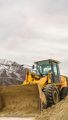 Vertical Bulldozer at a construction site against snowy mountain and cloudy sky in winter