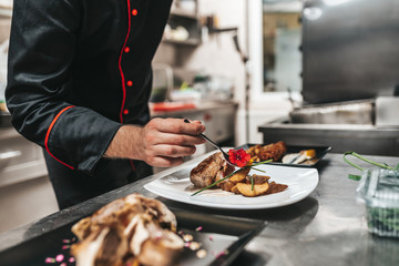 Professional chef arranging food plate with meat and vegetables.