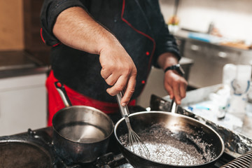 Professional chef in kitchen restaurant preparing sauce.