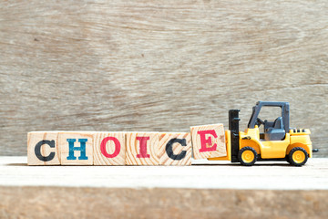 Toy forklift hold letter block e to complete word choice on wood background