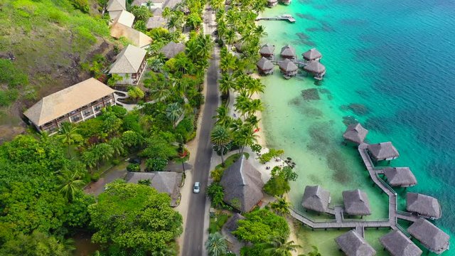 Aerial of cars driving on a coastal road on a beautiful tropical island, drone flying forward along the road - Bora Bora, French Polynesia