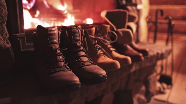 Winter Boots Drying in front of a Burning Fireplace in a cabin. 4K Stabilized shot. Family vintage folk boots standing near the fireside. Warm cozy fireplace in the authentic chalet. 
