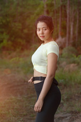 Young Asian woman runner does stretching and warm up exercise before trial running in nature forest in the morning. Sporty young female working out in forest. Weight Loss. Health care and lifestyle.