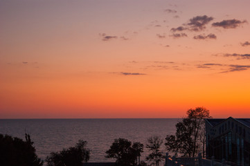 Sunset over the sea - view of a pink sky with purple clouds and contrasting trees. Subtropics, summer, heat, rest, vacation, relaxation, evening, night.