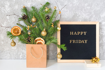 Happy Friday text on black letter board and festive bouquet of fir branches with christmas decor in...