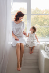 Mom and daughter are sitting on the windowsill and looking at each other with love. Mother's love.