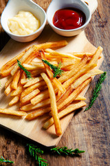 Crispy fry fries placed on a wooden chopping board with two dipping sauces, mayonnaise, tomato sauce