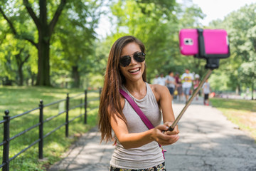 New York City tourist taking selfie stick photo in Central park, NYC. Happy travel Asian girl...