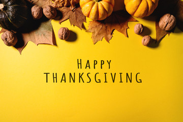 Happy Thanksgiving Day with maple leaves, nut and pumpkin on yellow background