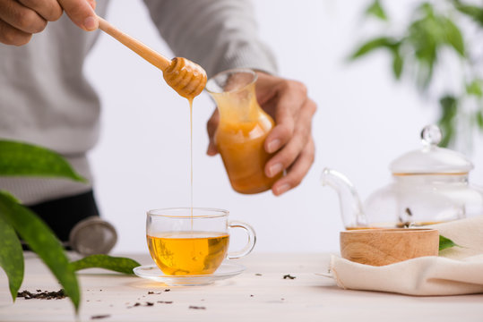 Cropped image of arista pouring honey into cup of tea