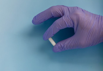 Hand in medical glove with pills on blue background