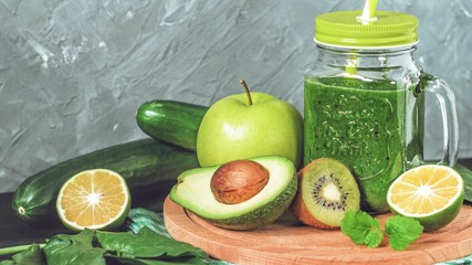 healthy green smoothie with ingredients on a wooden table: apple, kiwi, lime, spinach, mint, avocado, cucumber