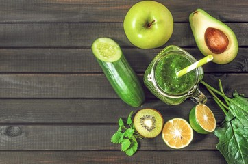 healthy green smoothie with ingredients on a wooden table: apple, kiwi, lime, spinach, mint, avocado, cucumber