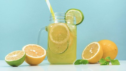 Lemonade drink of soda water, citrus and mint on the light blue background. Cocktail glass with handle and straw, sliced lemon and lime, front view