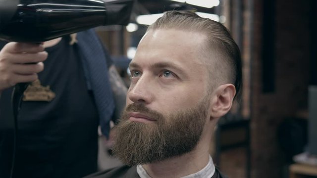 Young handsome bearded man at barbershop, shallow depth of field. Drying hair process