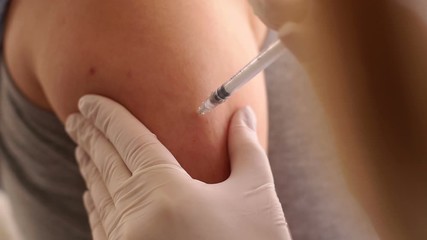 Doctor makes vaccination in the shoulder of patient in a hospital. Doctor vaccinating female patient in clinic. - Powered by Adobe